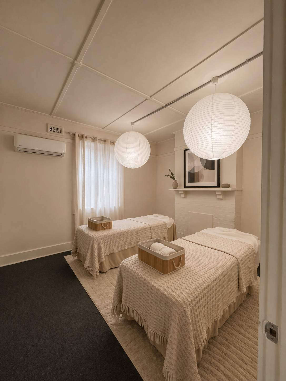 Double treatment room with two beds, two paper-lantern pendants, cream throws and a framed landscape